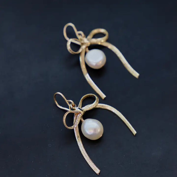 From Katie Waltman, these are the  Sloane Ribbon and Pearl Earrings – Elegant Gold Ribbon Earrings with Delicate Pearl Detail | Timeless & Feminine Jewelry for Chic, Sophisticated Style | Perfect for Weddings, Events & Everyday Elegance.