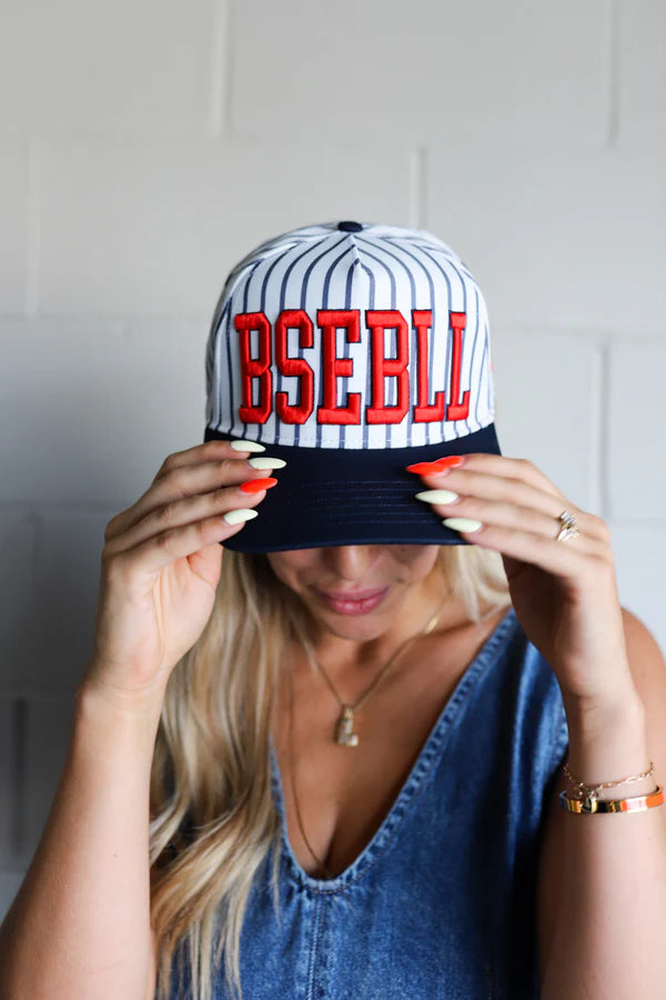 From KAXI this is a trending white and navy blue striped trucker hat. It features in bold red letters "BSEBLL".  Perfect for those warm summer nights.